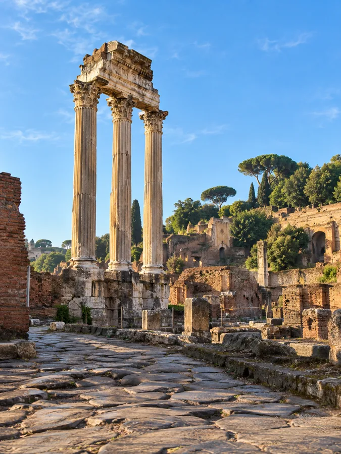 Three standing marble columns in the Roman Forum against a blue sky